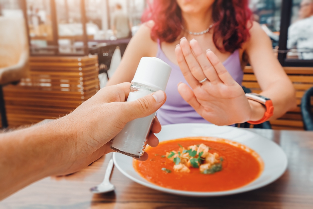  Woman refusing a salt shaker at a restaurant, emphasizing the importance of a low-salt diet for pre-surgery health and recovery.