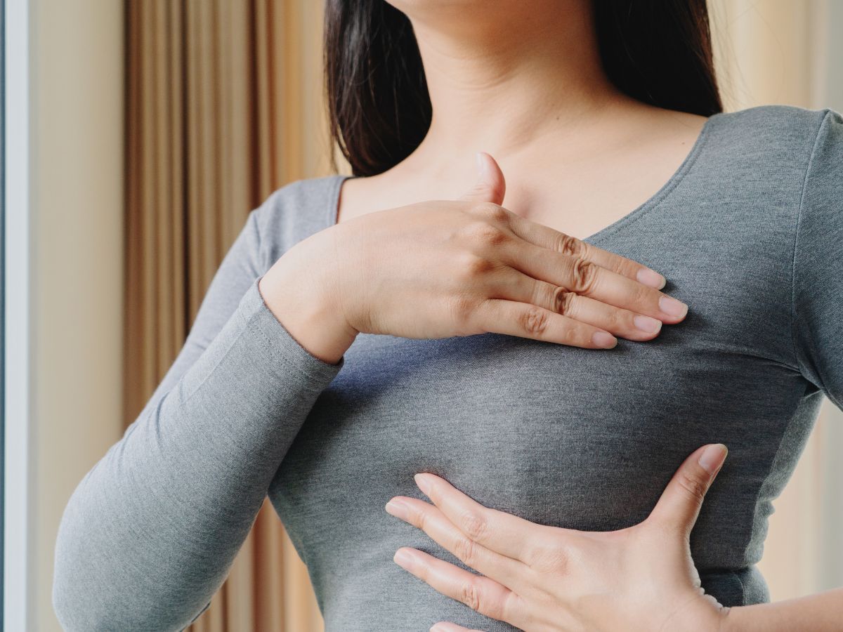 Woman examining her breasts for symptoms of capsular contracture, including tightness and misshapen appearance, after implant surgery.